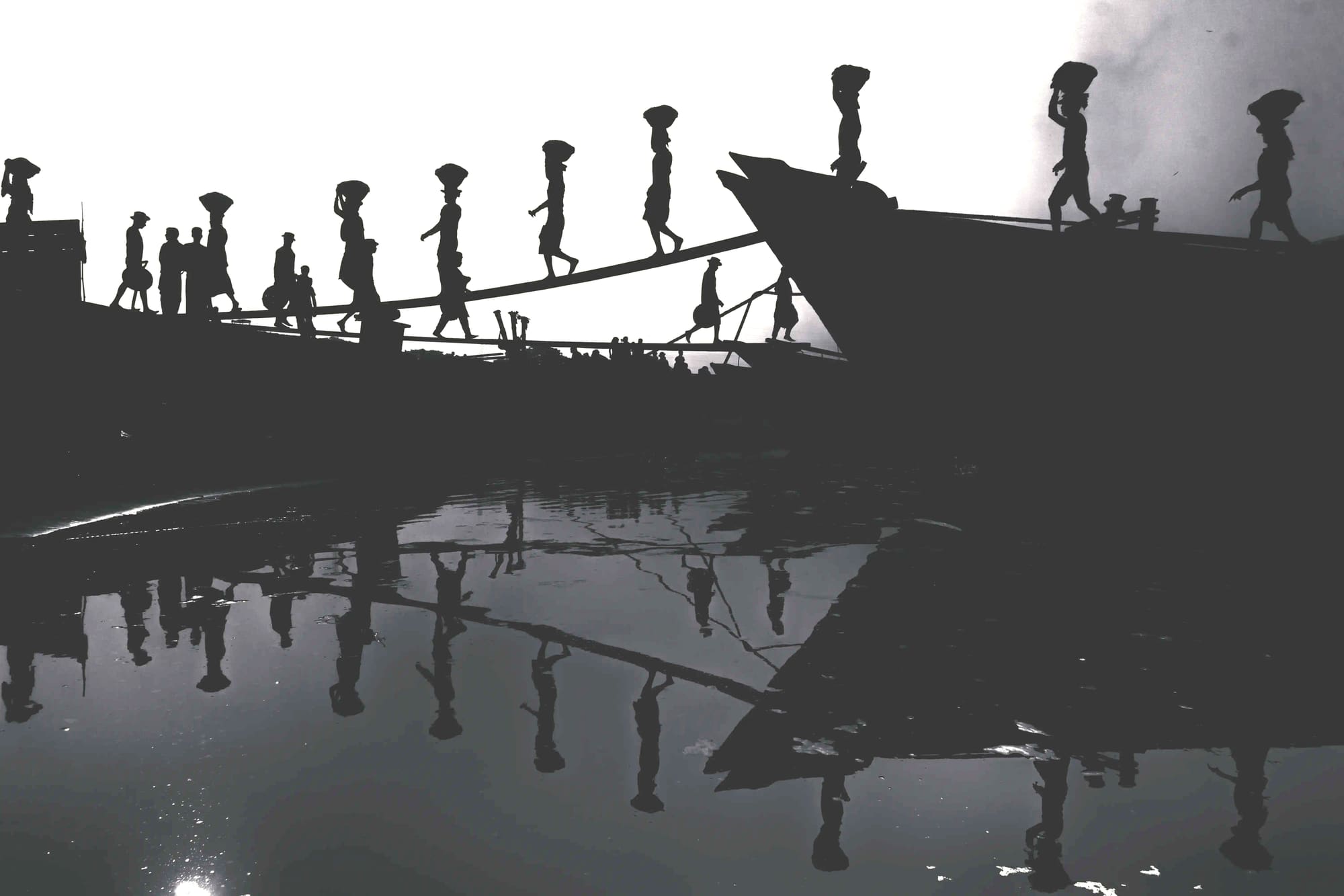 Silhouetted dock workers carrying baskets up a ship's gangway